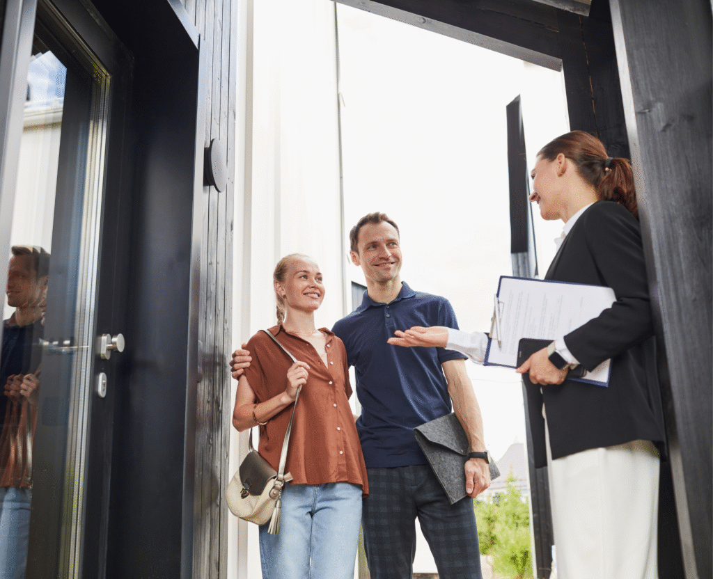 A couple stands at a doorway, smiling and listening to a woman with a clipboard who appears to be explaining aspects of property management Salem offers.